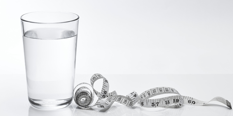 グラスに注がれた水と巻尺。水分補給とダイエットの関係性をイメージさせる構図